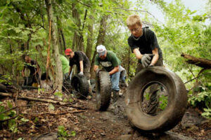 three people cleaning up tires in wooded area